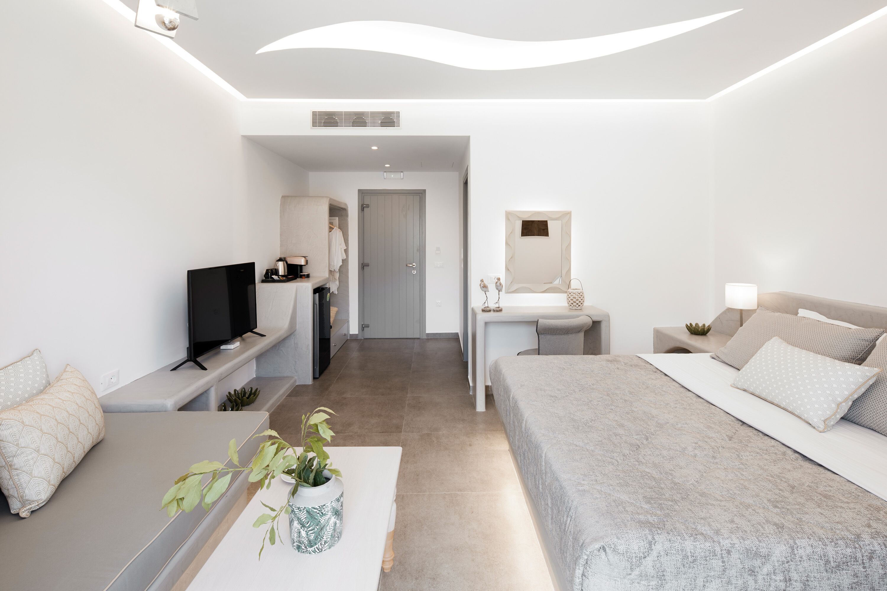 A modern hotel room with a bed, a desk, a TV, and a bathroom visible through an open door.