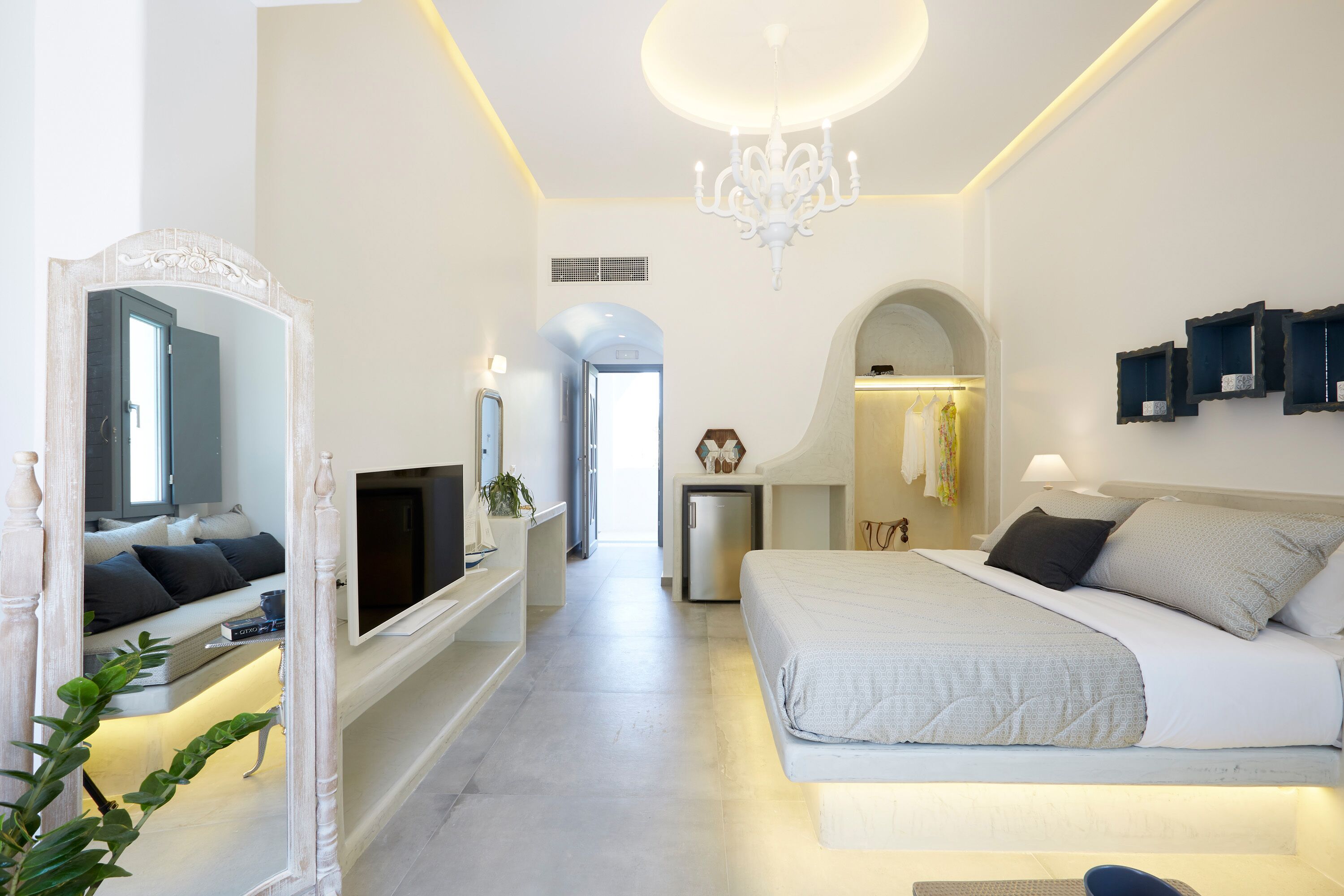 Una habitación de hotel moderna con una cama grande, televisión, espejo y candelabro.