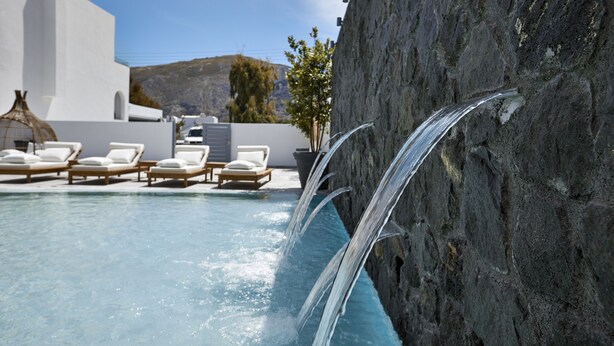 Ein Pool mit klarem Wasser, umgeben von weißen Wänden und Liegestühlen.