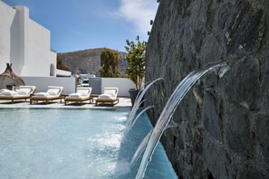 Una piscina con agua cristalina, rodeada de muros blancos y sillas de descanso.