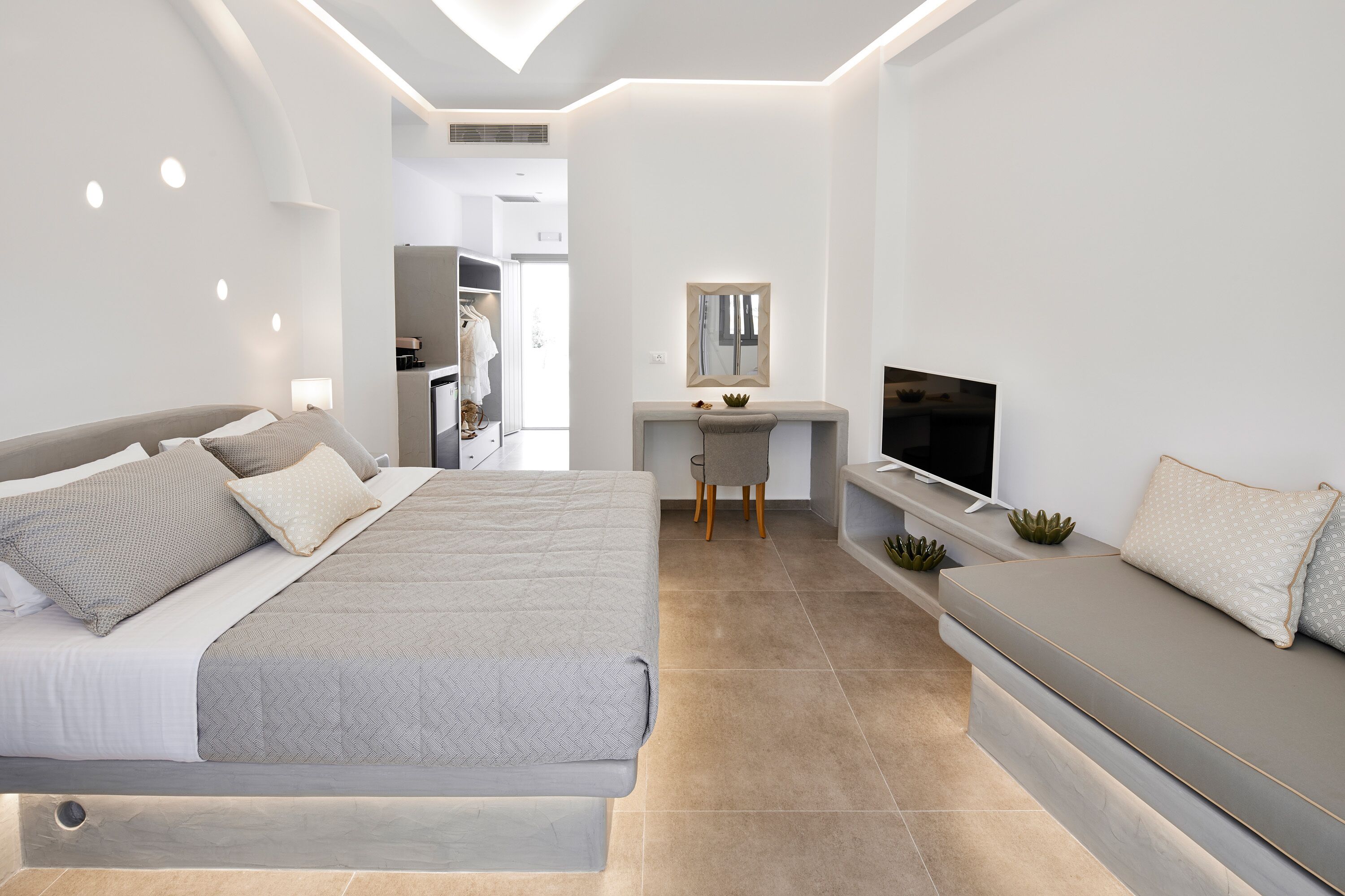 A modern bedroom with a large bed, a sofa, a desk, and a TV.