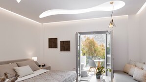Ein modernes Schlafzimmer mit Bett, Nachttisch und einer Sitzecke mit Blick ins Freie.