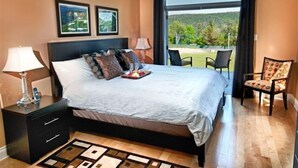 Un dormitorio con una cama grande, una mesita de noche, una silla y vistas al exterior.