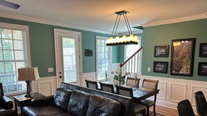 A living room with a leather sofa, dining table, chairs, a chandelier, and framed pictures on the wall.