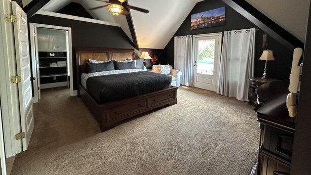 A bedroom with a sloped ceiling, a bed, a nightstand, a lamp, a closet, and a window with curtains.