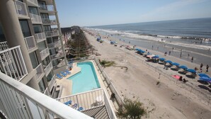 Un hotel con piscina, vistas a la playa, varios balcones y sombrillas.