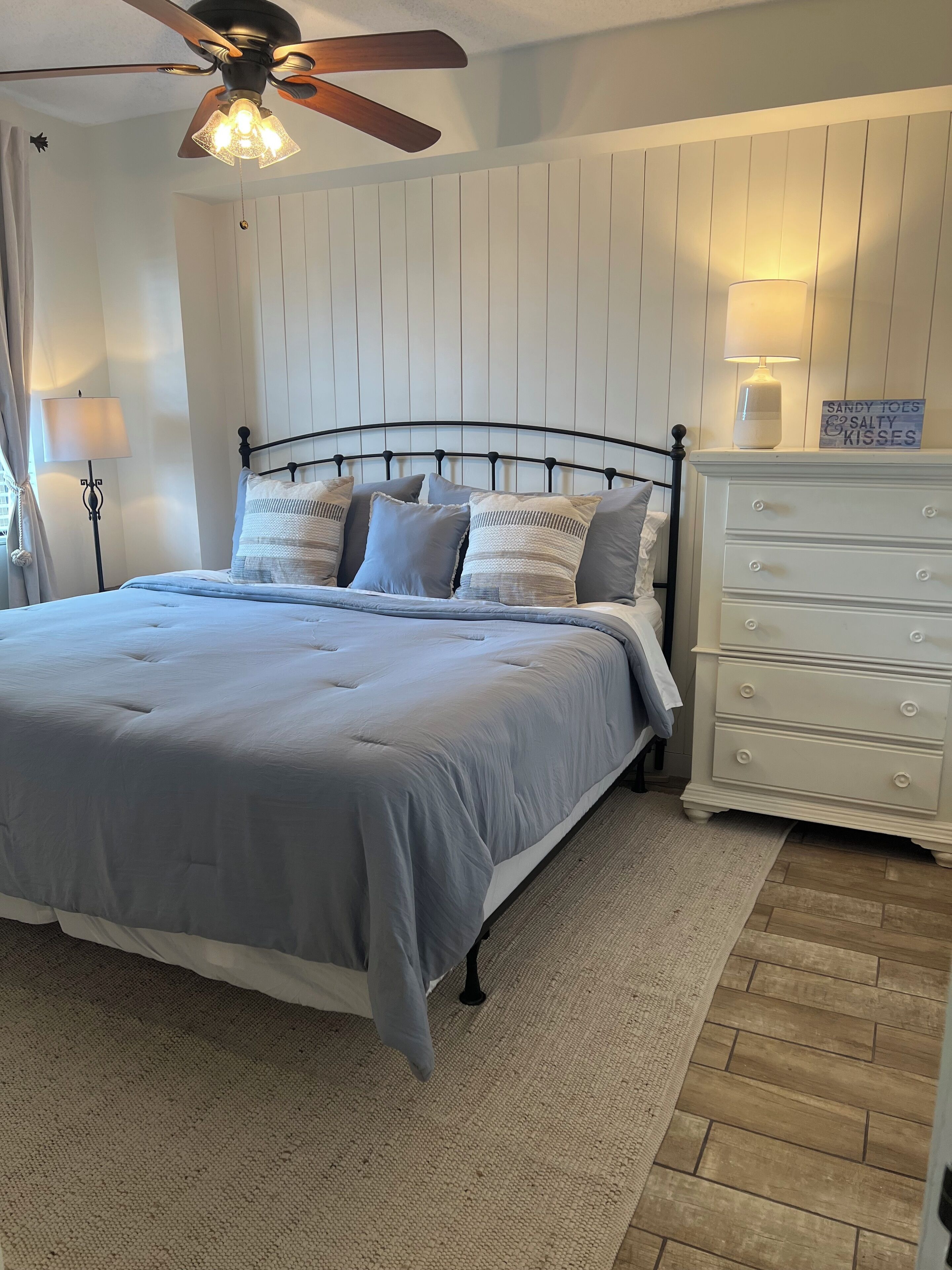 A bedroom with a bed, a nightstand, a dresser, a ceiling fan, and a wall-mounted lamp.