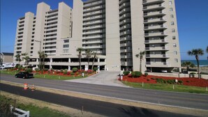 Un hotel de varios pisos con entrada central, zona de estacionamiento y vistas al océano.