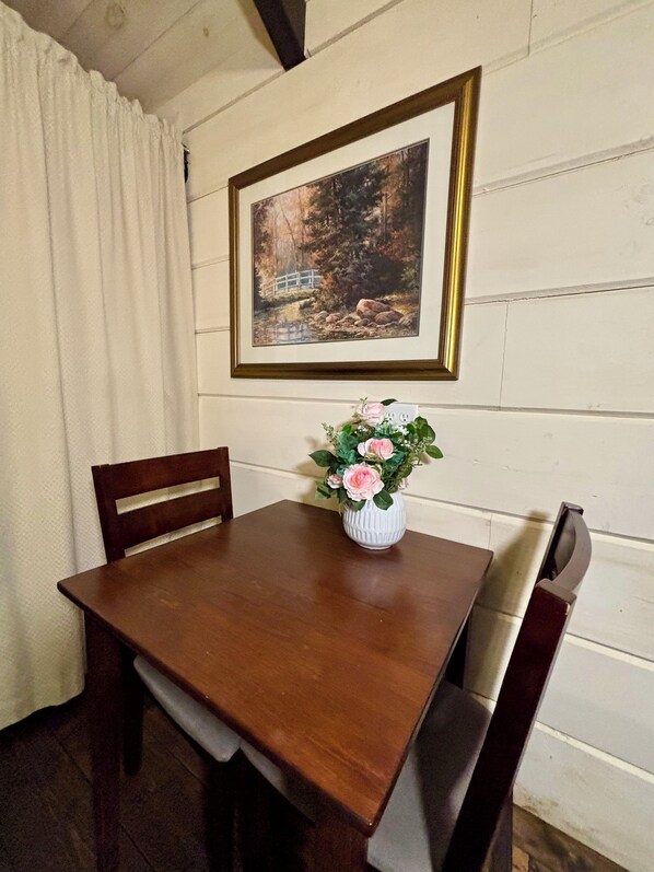 Ein Holztisch mit einer Blumenvase, ein gerahmtes Gemälde an der Wand und ein Holzstuhl.