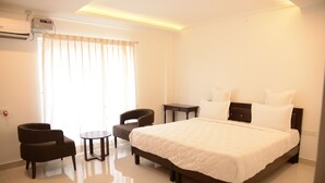 A hotel room with a large bed, a small table, two chairs, and a window with curtains. - Hotel RR Grand (Bengaluru)