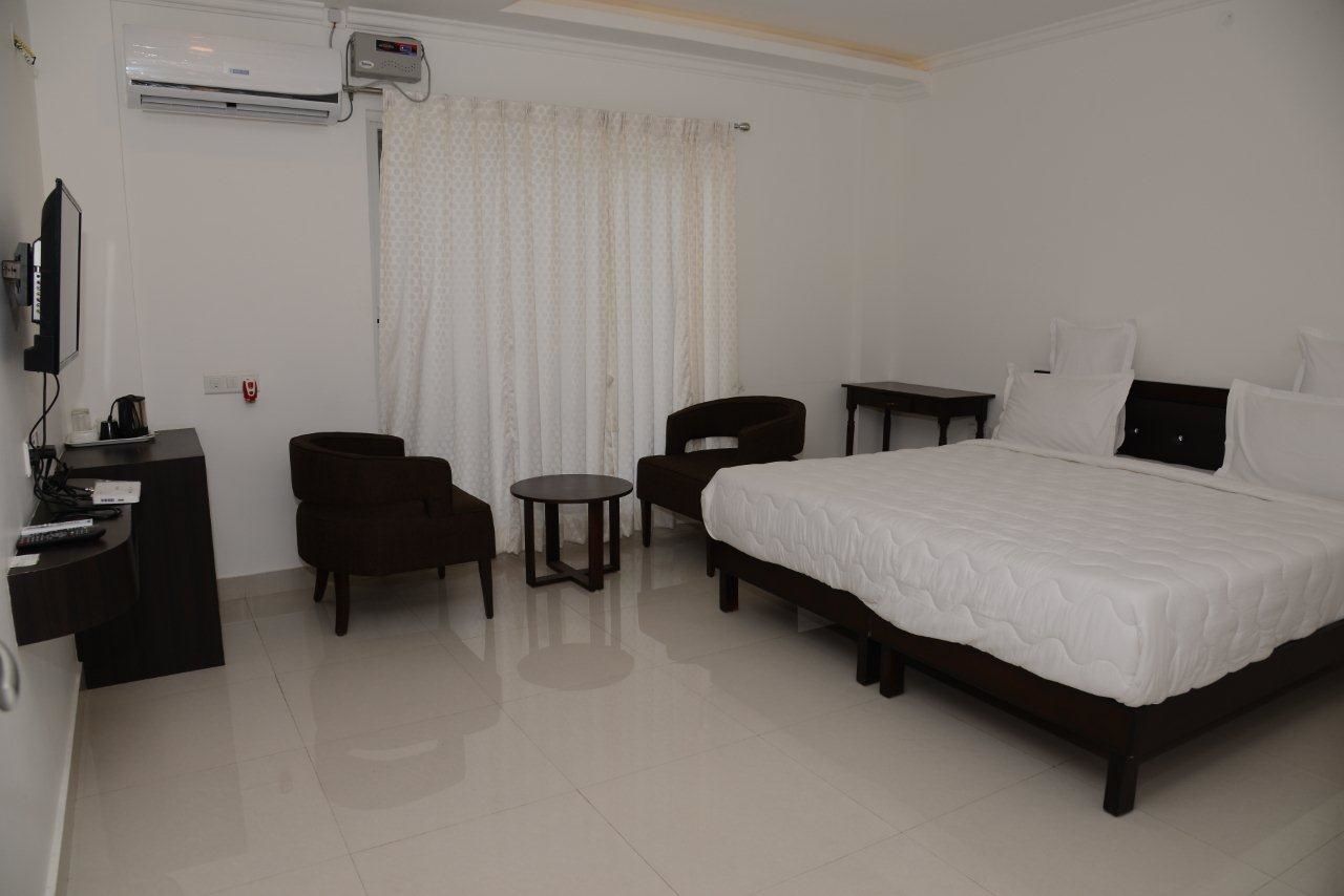 A hotel room with a large bed, a desk with a chair, a small round table, and a TV.