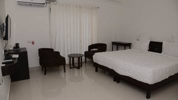 A hotel room with a large bed, a desk with a chair, a small round table, and a TV.