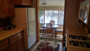A compact kitchen with wooden cabinets, a refrigerator, a gas stove, and a dining area with a table and chairs.