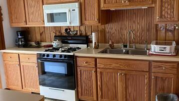 Une cuisine avec des meubles de rangement en bois, un four à micro-ondes, une cuisinière, un évier et une poubelle.