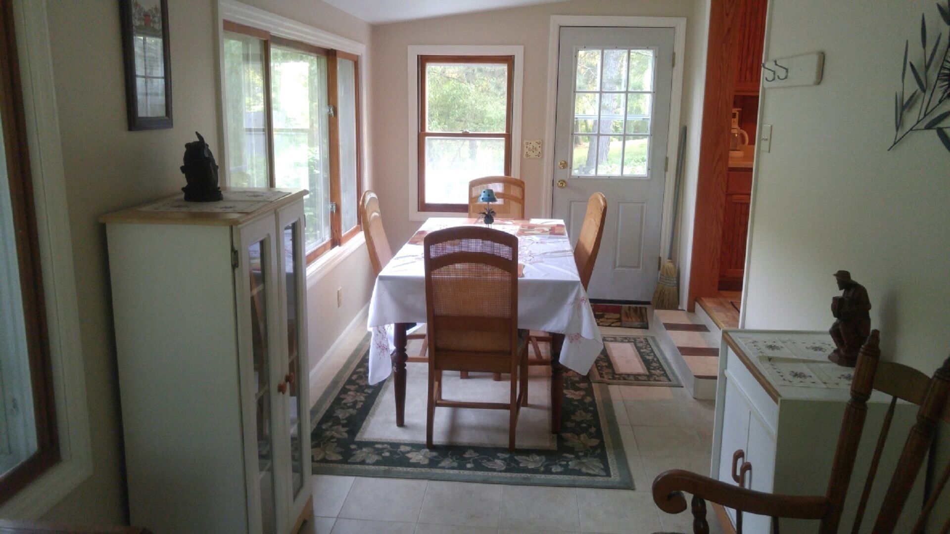 A dining area with a table set for two, a wooden chair, a cabinet, and a door leading outside.
