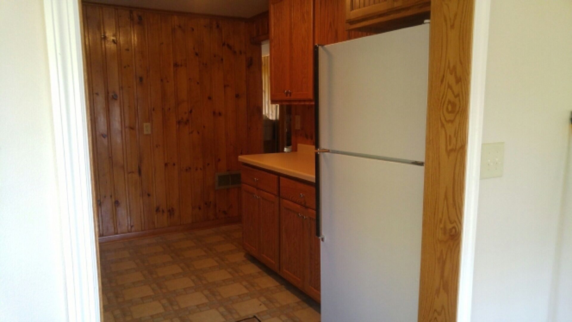 A small kitchen with wooden cabinets, a white refrigerator, and a checkered floor.