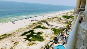 A beach view with a wooden deck, a pool, and a beach area with umbrellas.