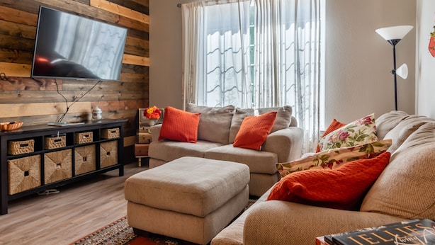 Un salon avec un téléviseur à écran plat fixé à un mur en bois, un ensemble de canapés, une table basse et une lampe sur pied.