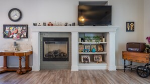 Un salon doté d’une cheminée, d’un téléviseur fixé au mur et d’un plancher en bois.