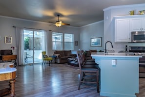 A spacious living area with a kitchen, wooden flooring, a ceiling fan, and a dining table.