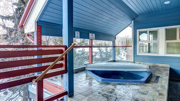 A covered outdoor area with a hot tub, a wooden bench, and a window.