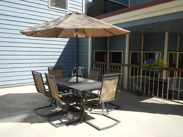 Un patio al aire libre con una mesa de metal y cuatro sillas, una sombrilla y una barandilla con jardineras.