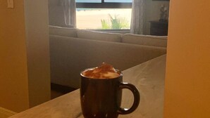 Una habitación con vistas a la playa a través de una ventana, un sofá y una taza sobre una mesa.