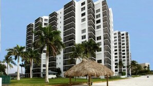 Un hotel moderno con varios pisos, palmeras y una estructura de techo de paja en la playa.