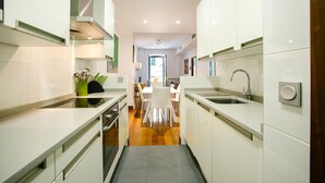 A modern kitchen with white cabinets, a central island, and a dining area with white chairs.