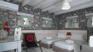 A room with stone walls, two beds, a glass table, a red chair, and a lamp. - ELIA village house . (Monastiraki ierapetra)