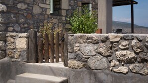 A stone building with a wooden fence, a small garden, and a view of the landscape. - ELIA village house . (Monastiraki ierapetra)