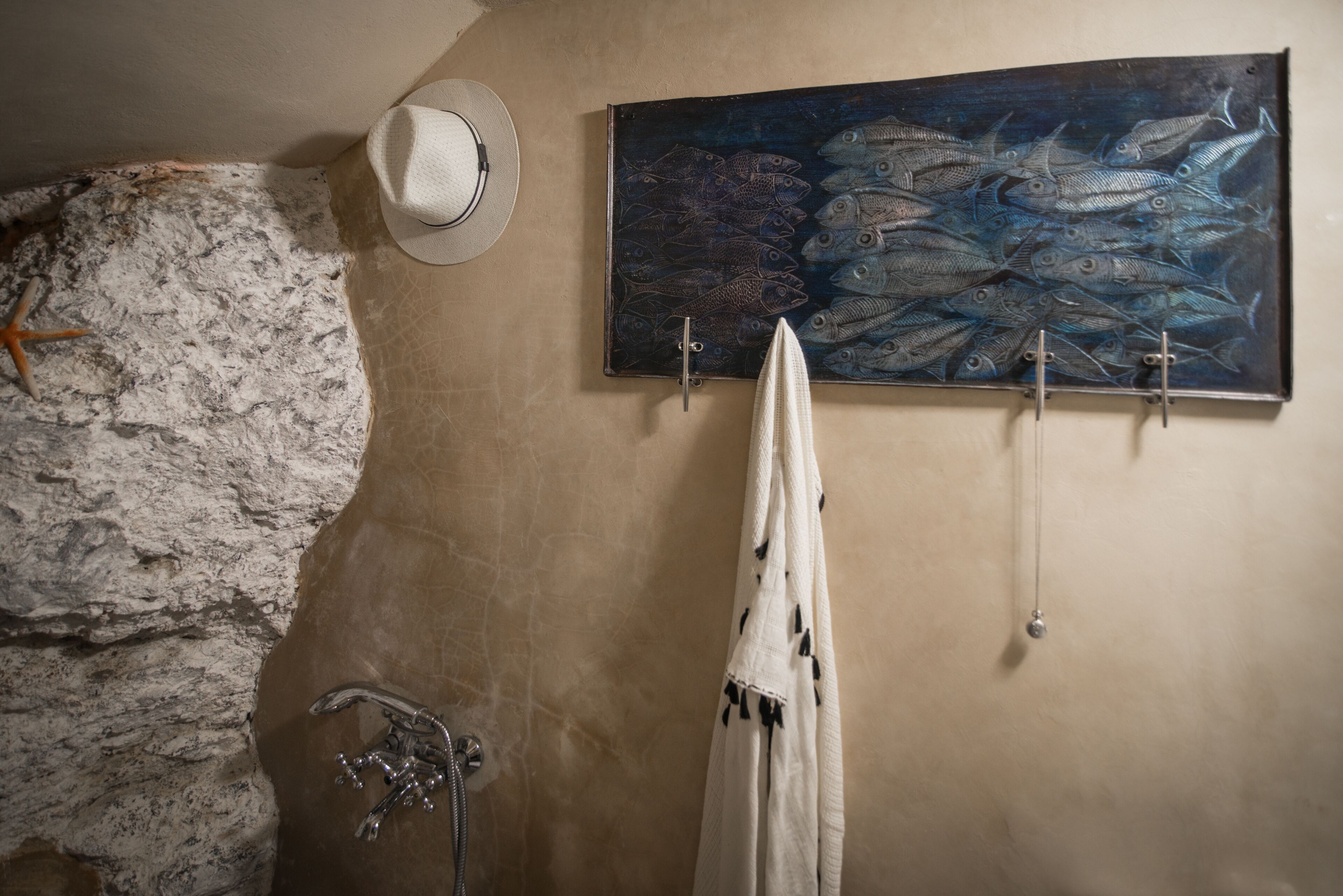 A bathroom with a stone wall, a white hat, a towel rack with a towel, and a painting of fish.
