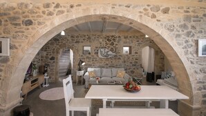 A stone-walled room with a white table and benches, a sofa, and a stone fireplace. - ELIA village house . (Monastiraki ierapetra)