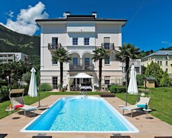 Un edificio grande de dos pisos con piscina, mobiliario exterior y palmeras.