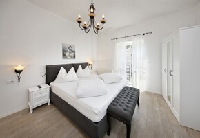 Un dormitorio con una cama grande, lámparas de noche, un candelabro, un banco y un armario.
