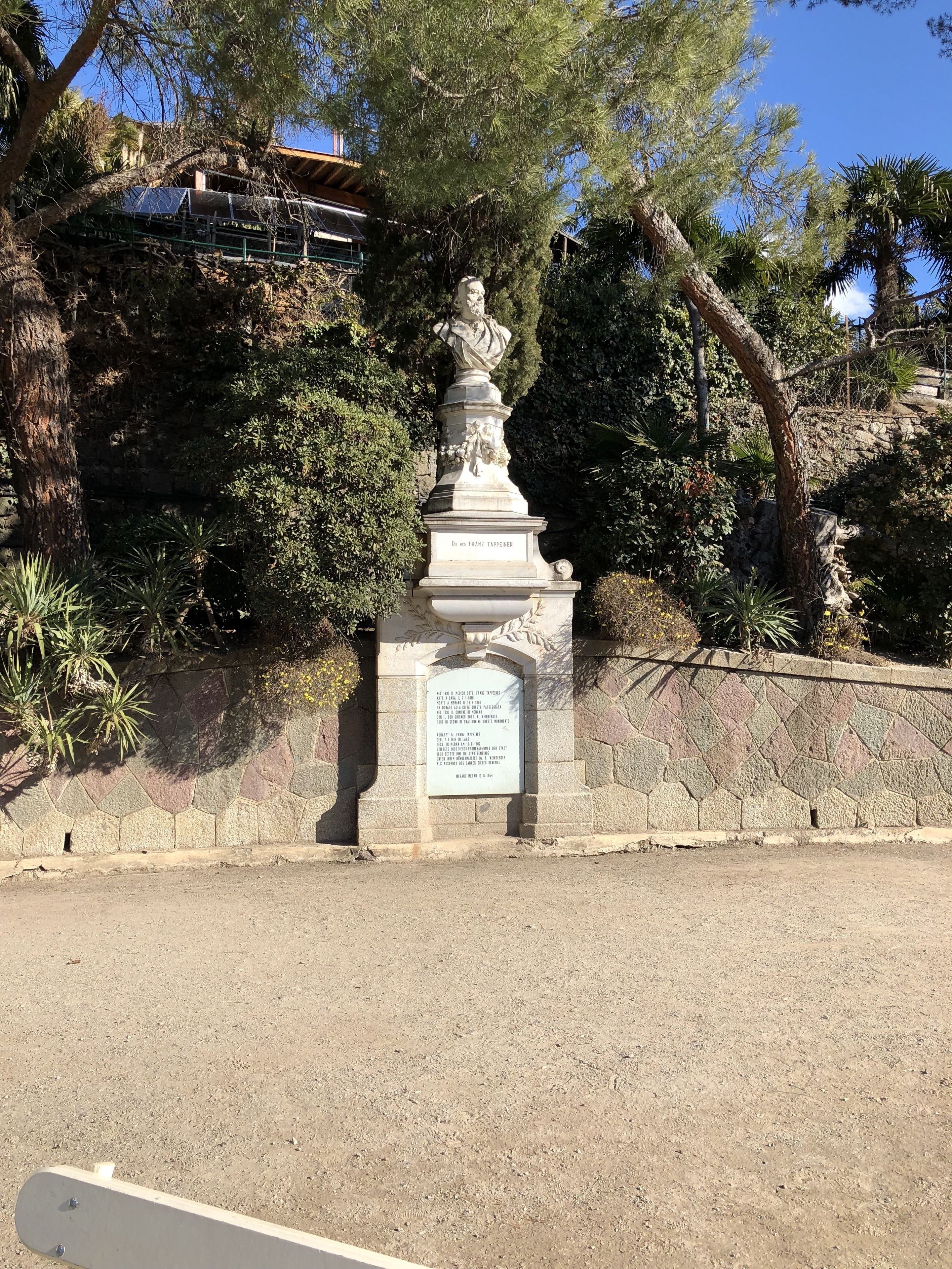 Ett stenmonument med inskriptioner, omgivet av träd och en stenmur.