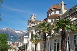 A historic building with classical architecture, including a dome and columns, in a town with a mountain backdrop.