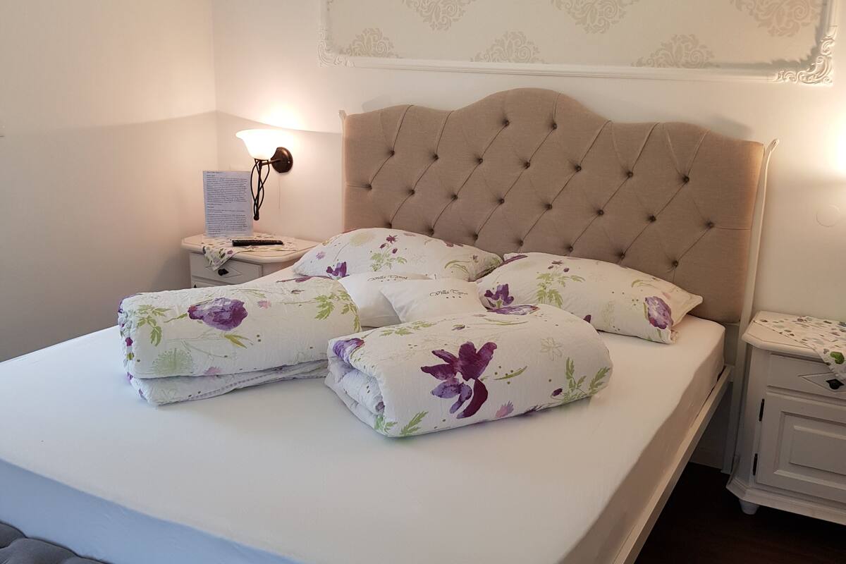 A neatly made bed with floral-patterned pillows, a tufted headboard, and a bedside table with a lamp.