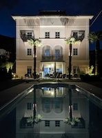 Un edificio de dos pisos con piscina frente a él, con balcones y mobiliario exterior.