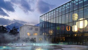 A modern building with large glass windows and a pool area with people swimming. - Garni Villa Tyrol - Adults Only (Merano)