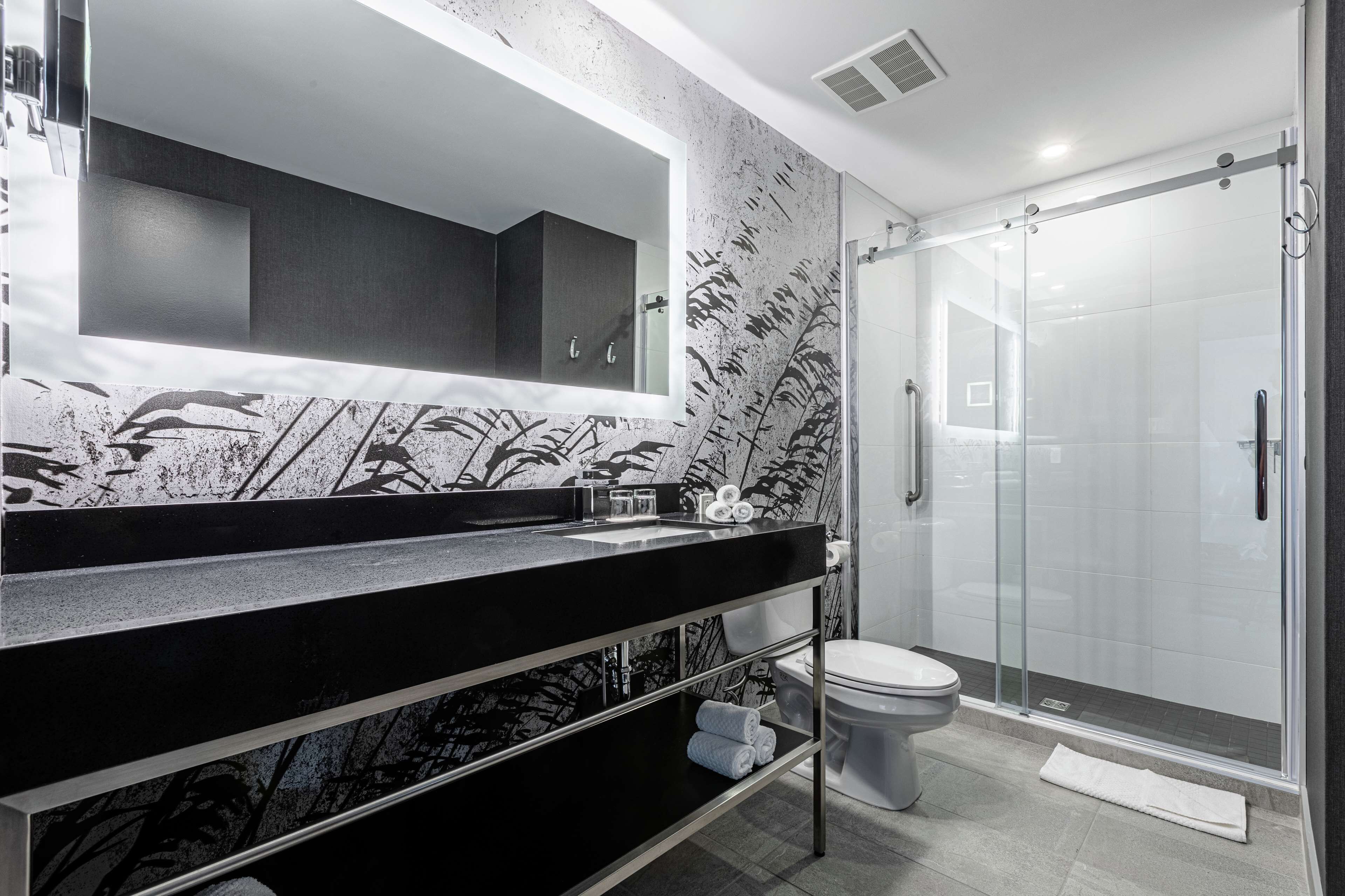 A modern bathroom with a black countertop, a large mirror, a glass shower enclosure, and a toilet.