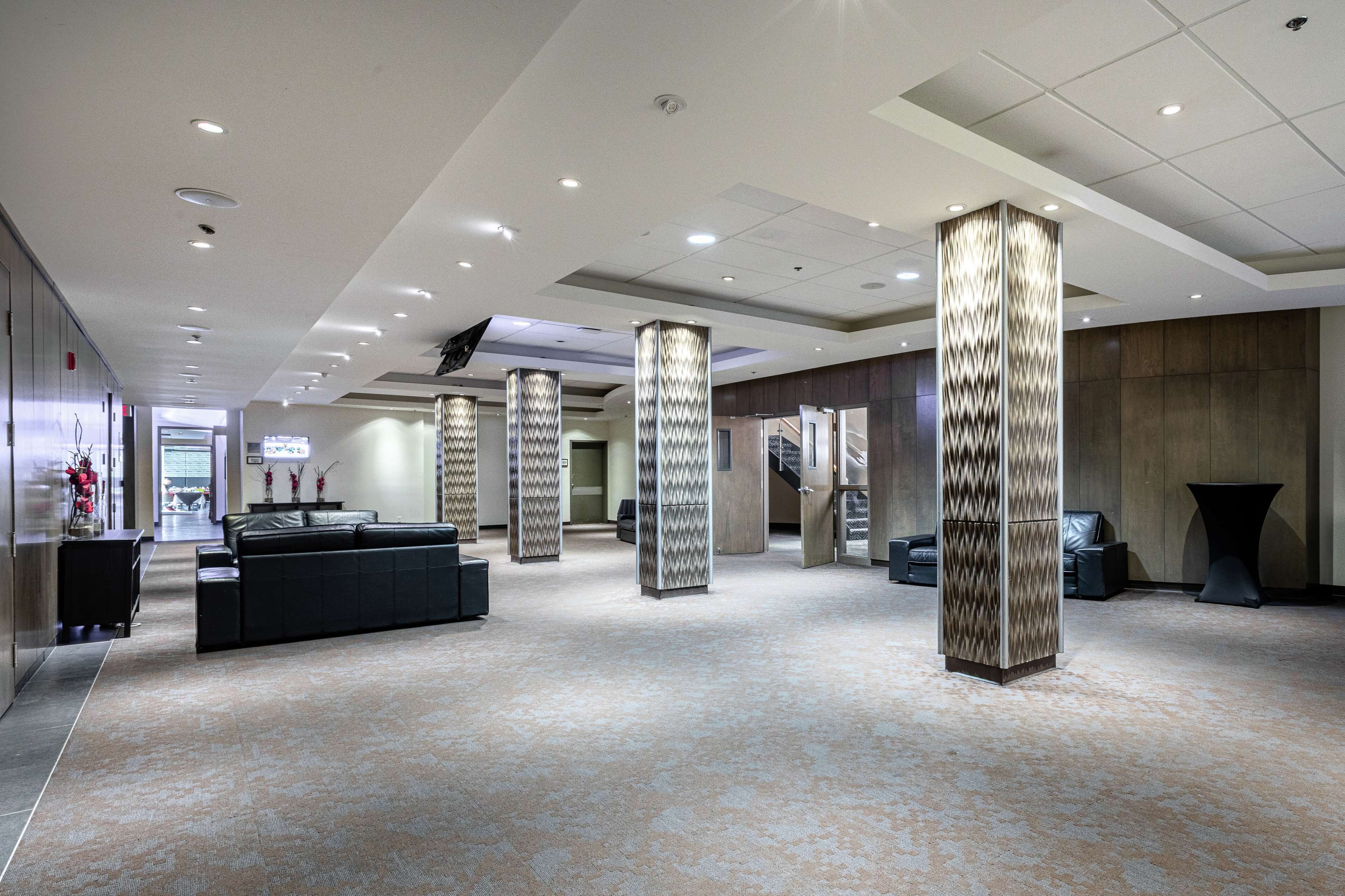 A spacious lobby with a modern design, featuring a black leather sofa, decorative pillars, and a carpeted floor.