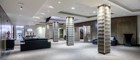 A spacious lobby with a modern design, featuring a black leather sofa, decorative pillars, and a carpeted floor.
