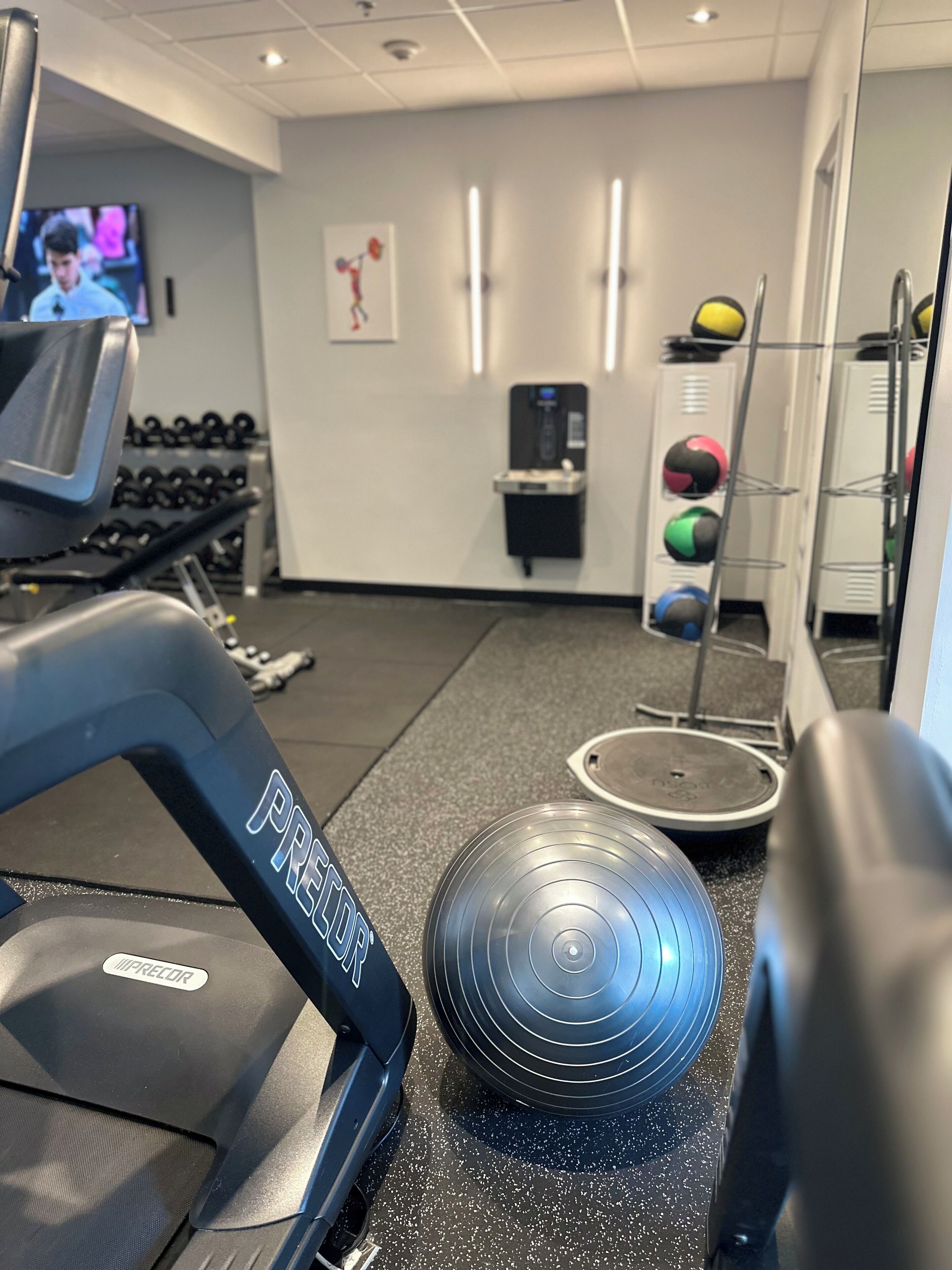 Une salle de sport équipée de tapis de course, d’un distributeur d’eau et de ballons d’exercice.