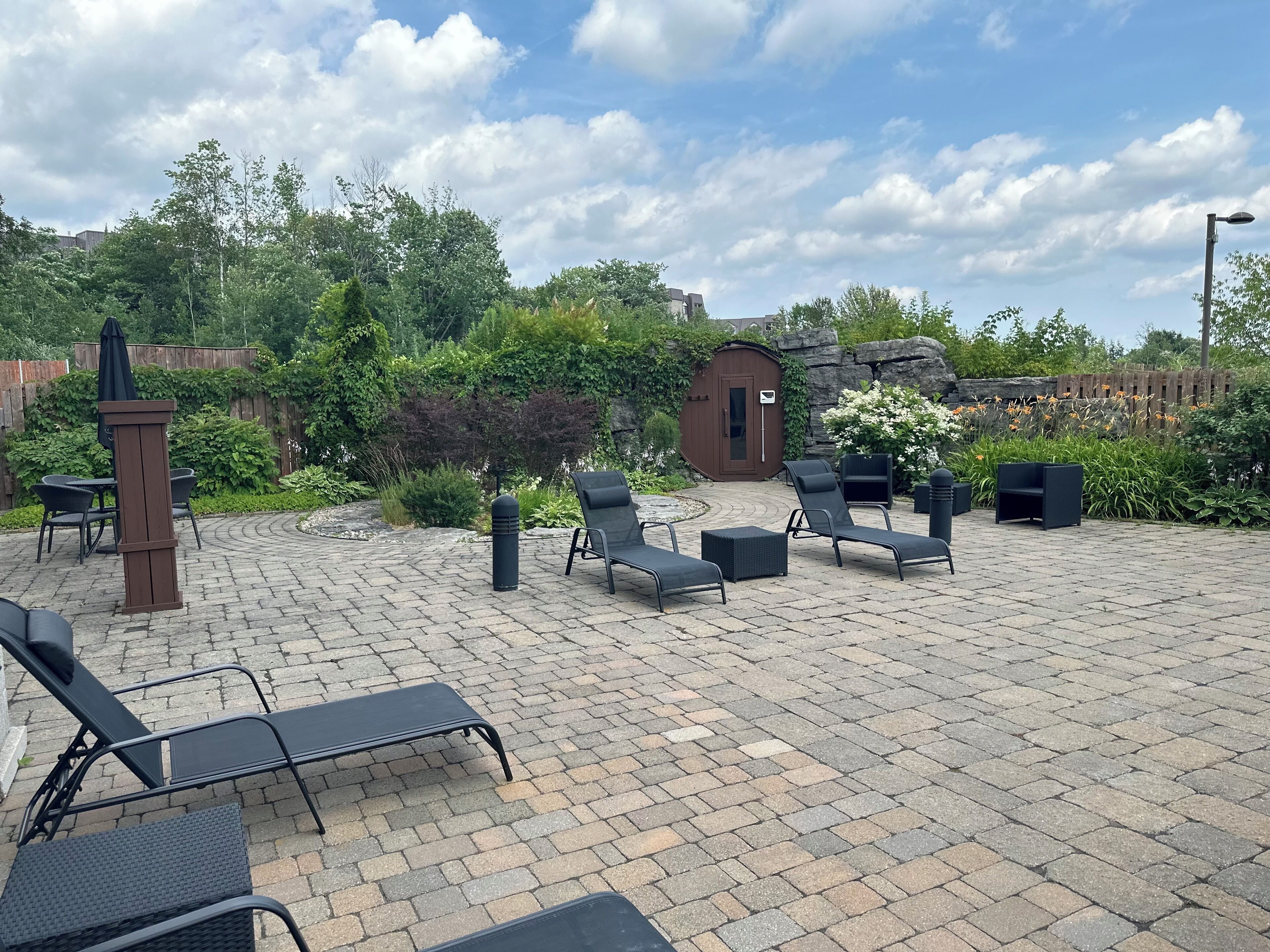 Un patio al aire libre con sillones de descanso, una mesa de madera y un pequeño jardín con un cobertizo de madera y un muro de piedra.
