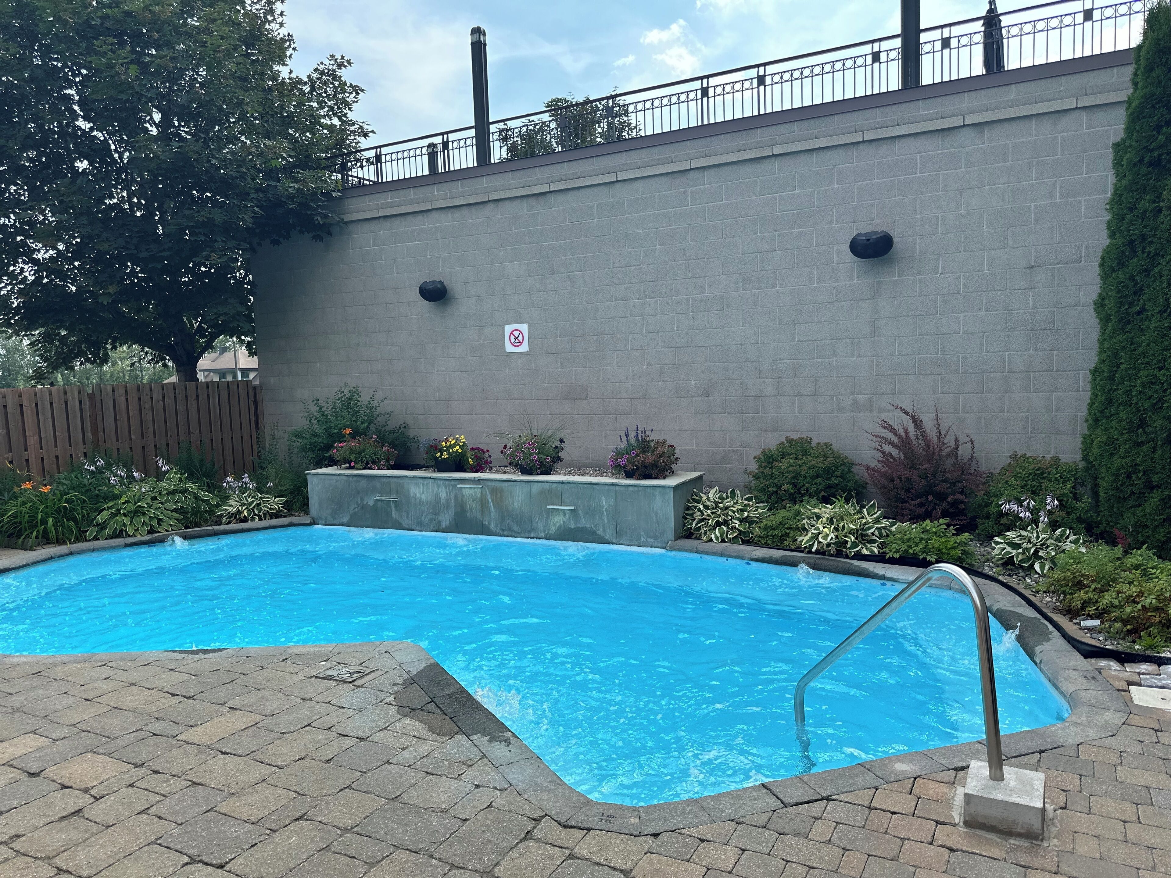 Una piscina rectangular con una escalera de metal, rodeada por una solana de ladrillo.