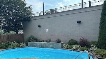 Una piscina rectangular con una escalera de metal, rodeada por una solana de ladrillo.