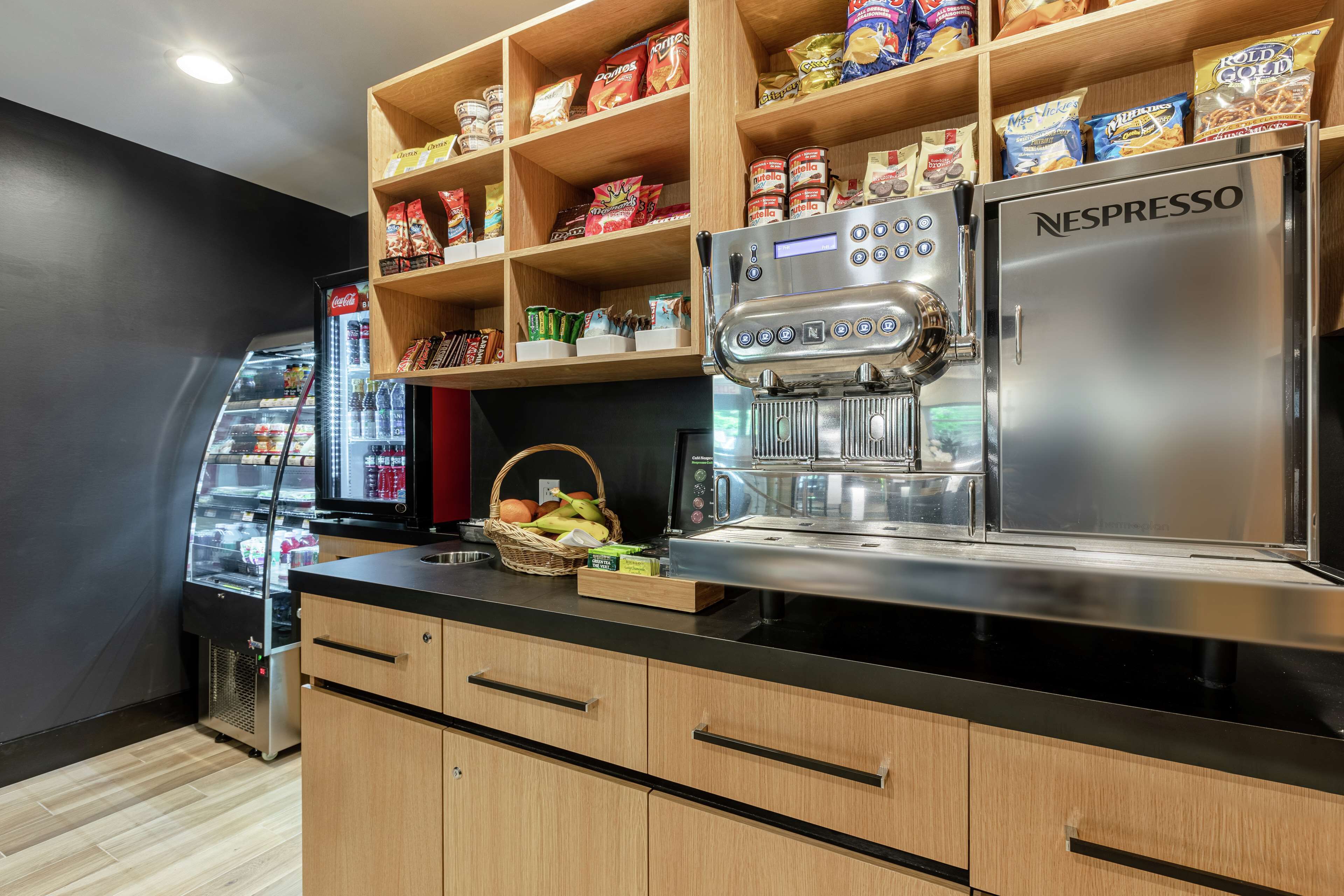 Una kitchenette con una máquina de café Nespresso, un refrigerador con aperitivos y una cesta de fruta.