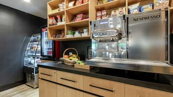 Una kitchenette con una máquina de café Nespresso, un refrigerador con aperitivos y una cesta de fruta.