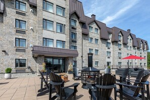 A stone building with multiple windows and a covered outdoor seating area with chairs and a fire pit.